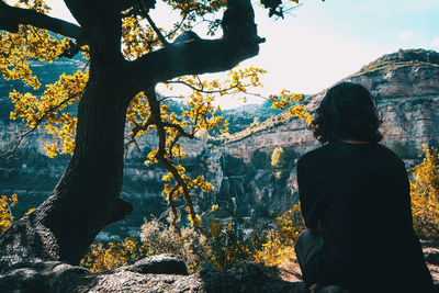 A girl with her back sitting under the shade of a tree enjoying the landscape relaxed