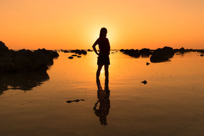 Silhouette woman standing at beach against sky during sunset