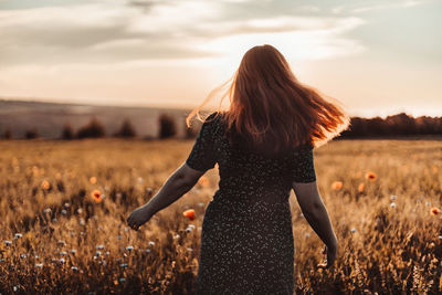 Woman standing on field against sky during sunset