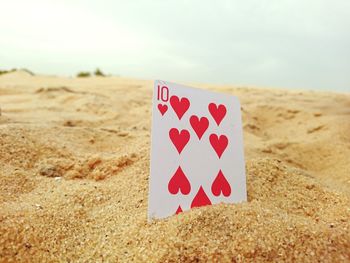 Close-up of card on sand against sky