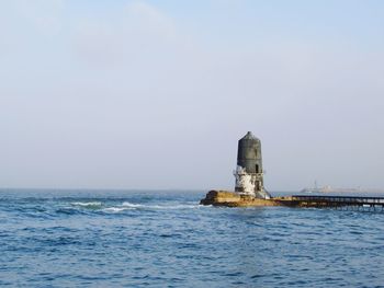Lighthouse by sea against clear sky