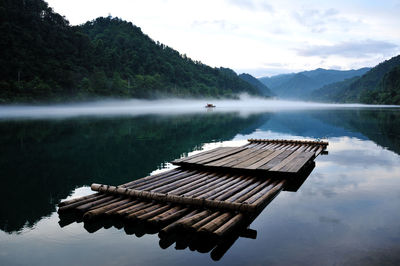 Wooden raft on lake amidst mountains against sky