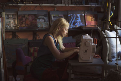 Side view of young fashion designer using sewing machine in studio