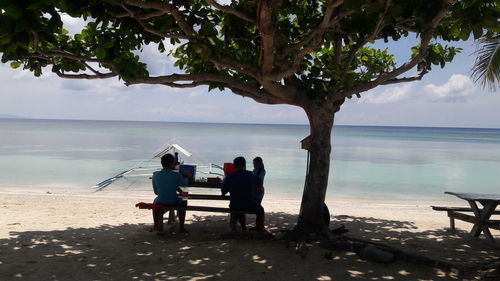 Rear view of people sitting on beach against sky