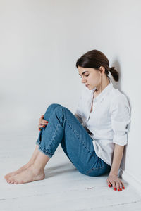 Young woman looking away while sitting against wall