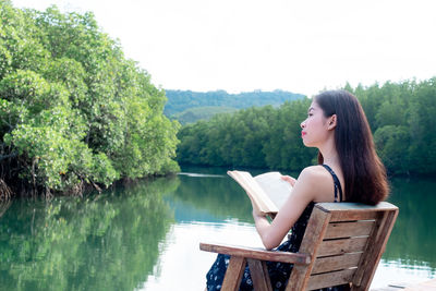 Woman sitting by lake against trees