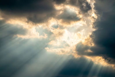 Low angle view of sunlight streaming through clouds