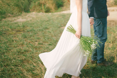 Low section of couple holding hands while standing on grassy field in park