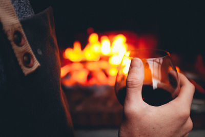 Midsection of person holding wineglasses against bonfire