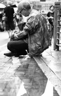 Man writing while sitting on sidewalk in city