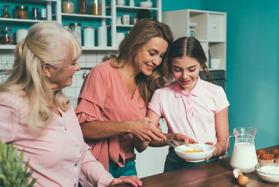 Cheerful daughter with parents preparing food at kitchen