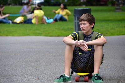 Teenage boy sitting on skateboard at park