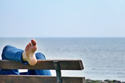 Low section of man relaxing by sea against clear sky