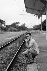 Thoughtful young man crouching on railroad station platform