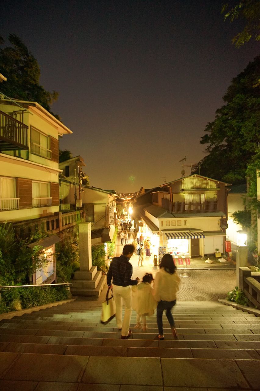 building exterior, architecture, walking, built structure, street, city, men, lifestyles, illuminated, person, city life, rear view, tree, the way forward, full length, night, road, sidewalk, sky