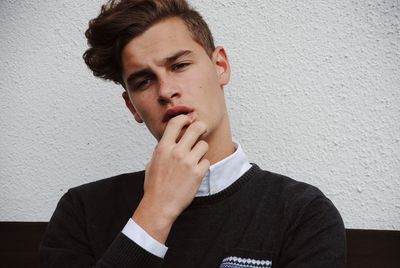 Thoughtful handsome man with fingers on lips against white wall