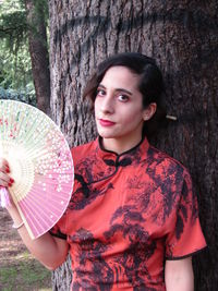 Portrait of young woman holding tree trunk