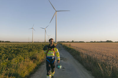 Technician walking on field path at a wind farm with climbing equipment