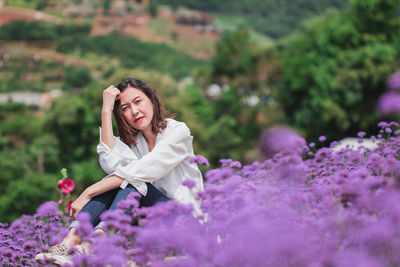Portrait of beautiful woman sitting by purple flowering plants
