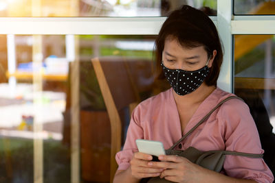 Woman wearing mask using smart phone standing outdoors