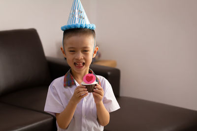 Portrait of boy holding cupcake at home