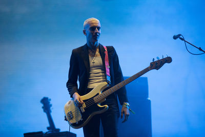 Full length of man playing guitar against blue sky