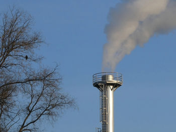 Smoke spews out of a chimney at an industrial plant near the trees with bird