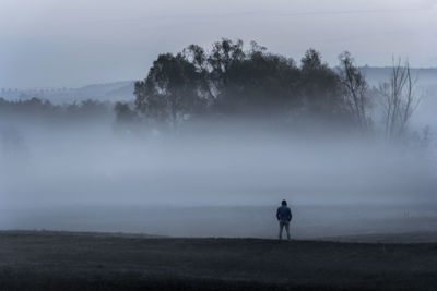 Rear view of man standing on field during foggy weather