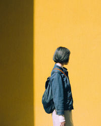 Rear view of woman standing against yellow wall