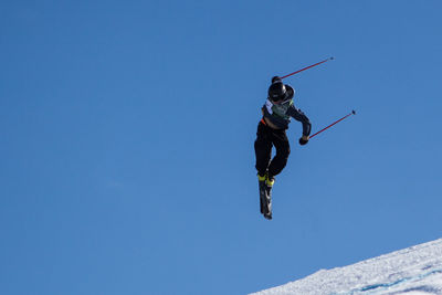 Low angle view of person jumping against clear blue sky