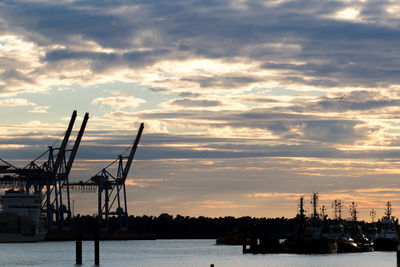 Cranes at commercial dock against sky during sunset