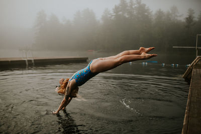Side view of woman jumping in lake during foggy weather