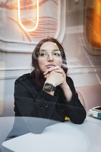 Young woman sitting in cafe seen through glass