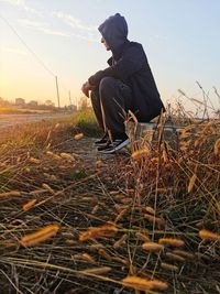 Side view of man sitting on field against sky