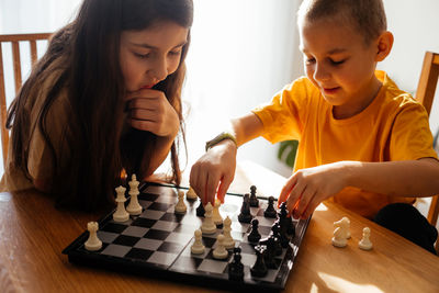 Smiling sibling playing chess at home