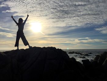 Silhouette woman standing on rock by sea against sky