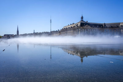 Reflection of building in lake against clear blue sky