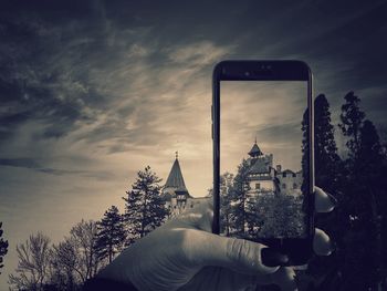 Hand holding smart phone against sky