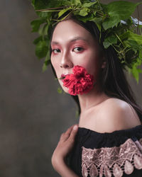 Portrait of a beautiful young woman standing by red flowering plant