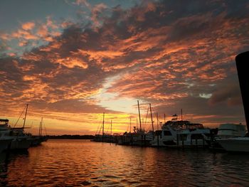 Sailboats moored in harbor during sunset