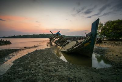 Boat moored at beach against sky during sunset