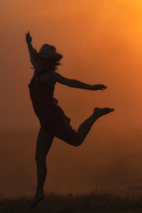 Silhouette woman dancing against orange sky during sunset