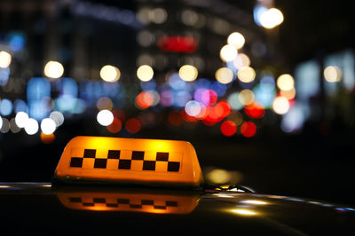 Close-up of taxi sign against defocused lights at night