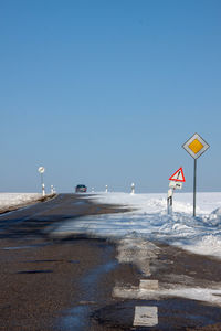 Road sign on snow covered land against clear sky