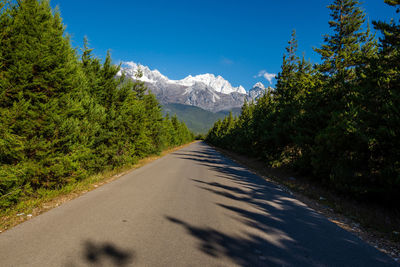 Road amidst trees and mountains against sky