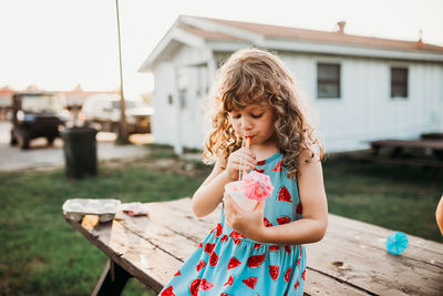 Preschool age girl sitting at picnic table drinking snow cone