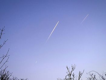 Low angle view of vapor trails against clear blue sky