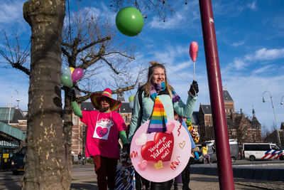 Rear view of smiling girl with balloons against sky in city