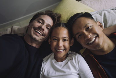 Directly above portrait of smiling gay couple lying down with daughter at home