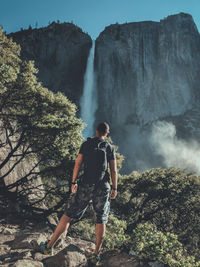 Rear view of man with backpack looking at waterfall